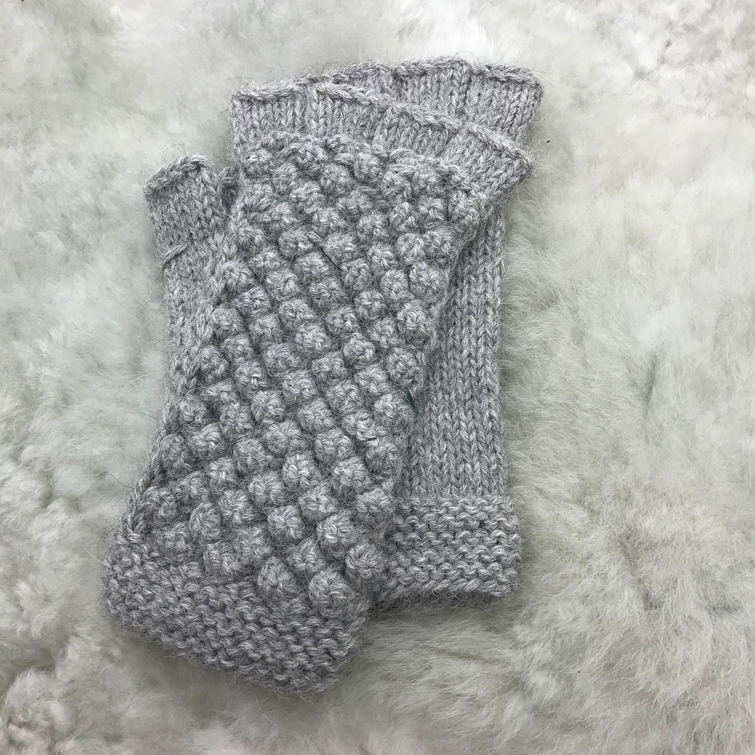 A pair of silver fingerless gloves made with a popcorn texture stitch, lying on a light gray background.